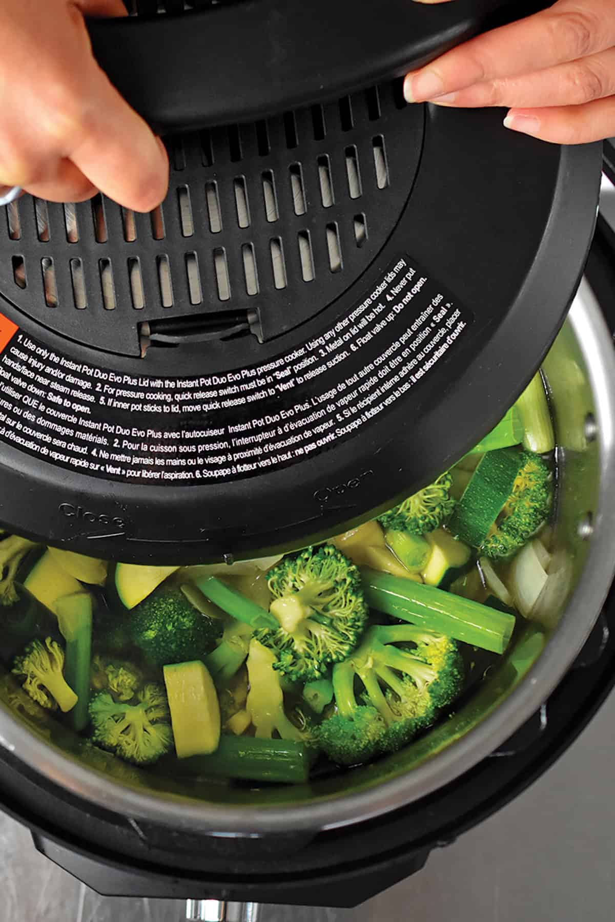 An overhead shot of someone putting the lid on top of an Instant Pot filled with the ingredients to make green soup.