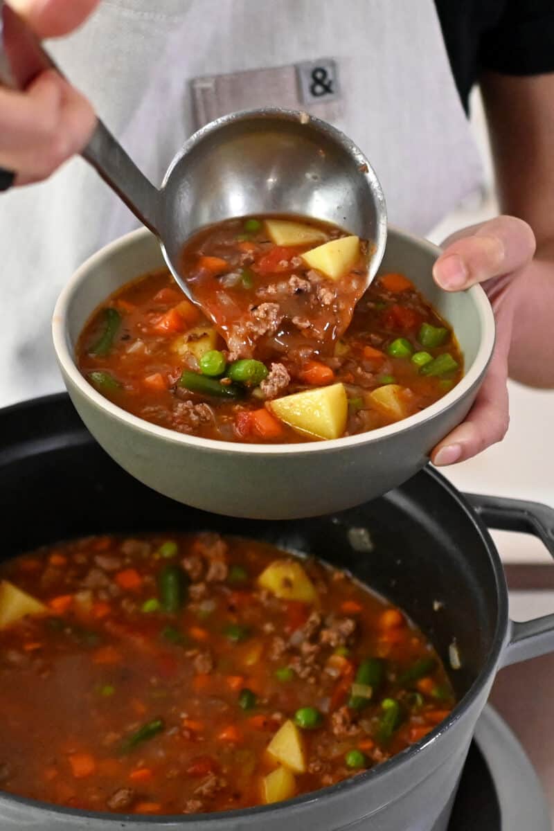 Someone in a white apron is ladling paleo hamburger soup into a soup bowl.