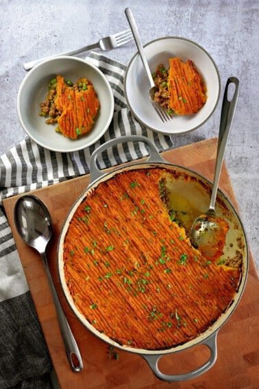 An overhead shot of an Indian-Spiced Shepherd's Pie in a cast iron skillet with two servings scooped out and in two small plates next to the pan.