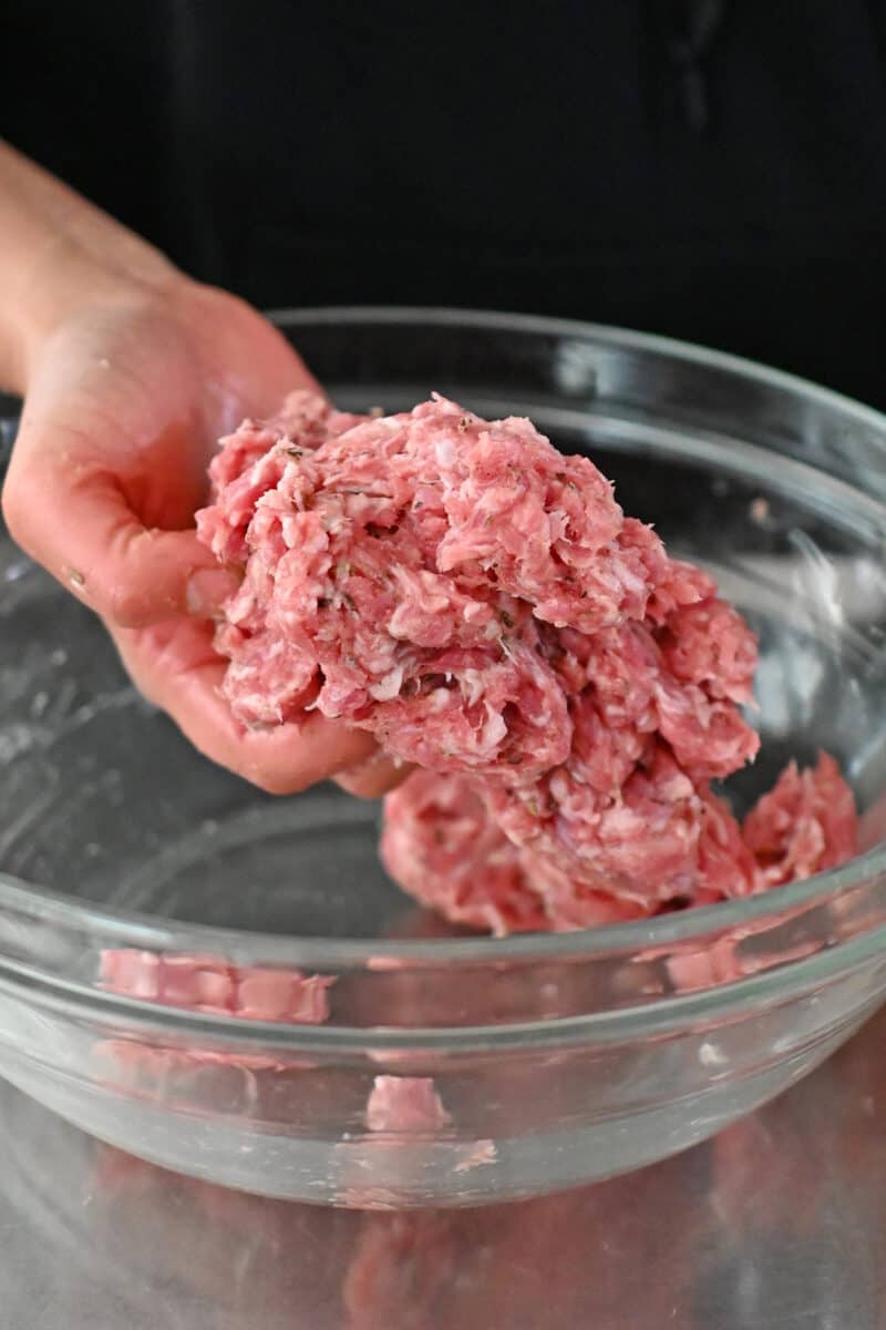 A hand is mixing homemade Whole30 Italian sausage in a clear glass bowl.