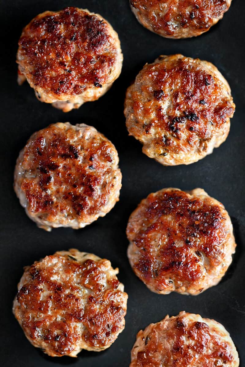 An overhead shot of golden brown homemade Italian sausage patties on a black plate.