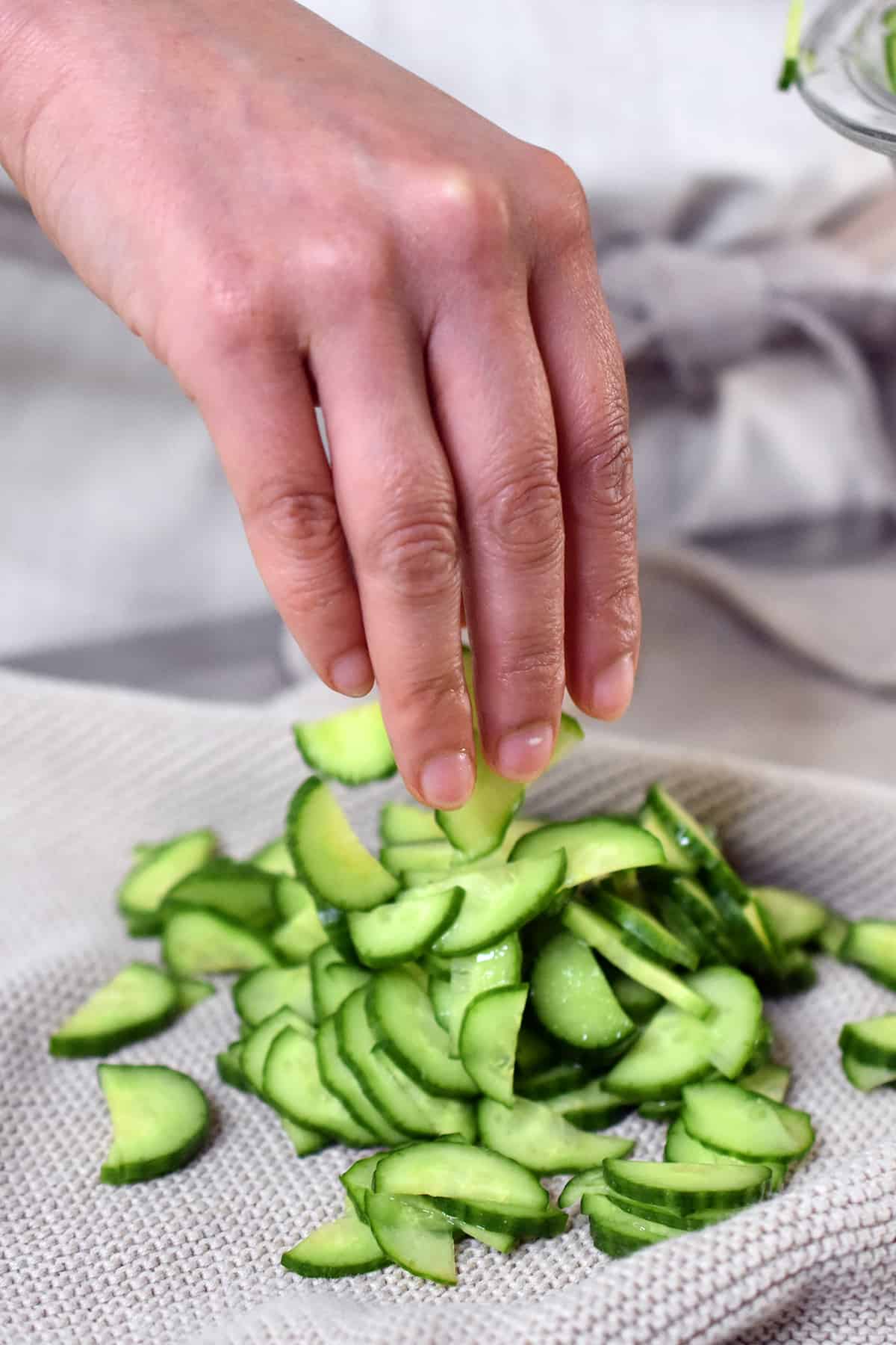 Placing salted thinly sliced Persian cucumbers onto a clean kitchen towel.