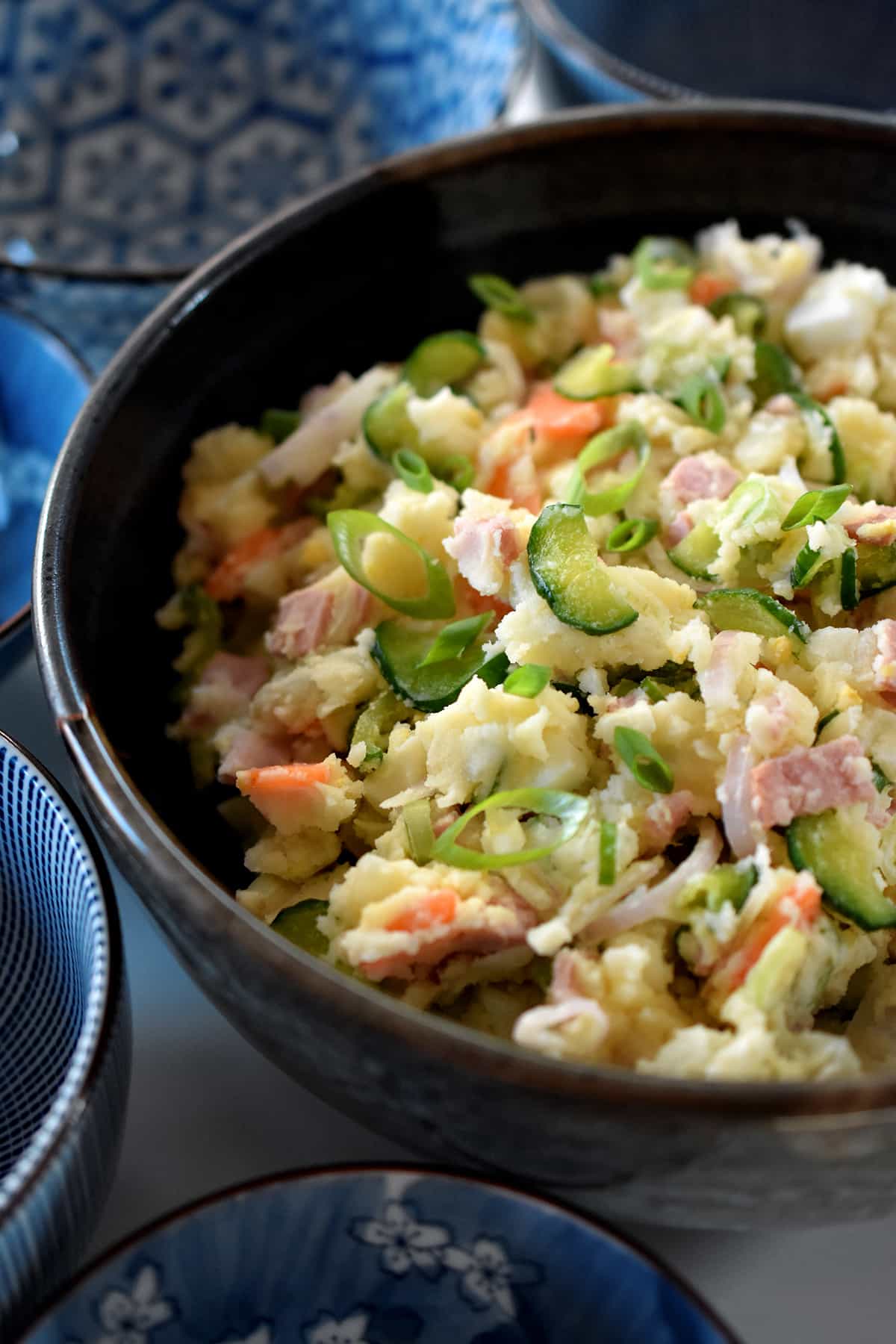 An overhead side view of a serving bowl of Japanese potato salad with small blue serving bowls next to it.