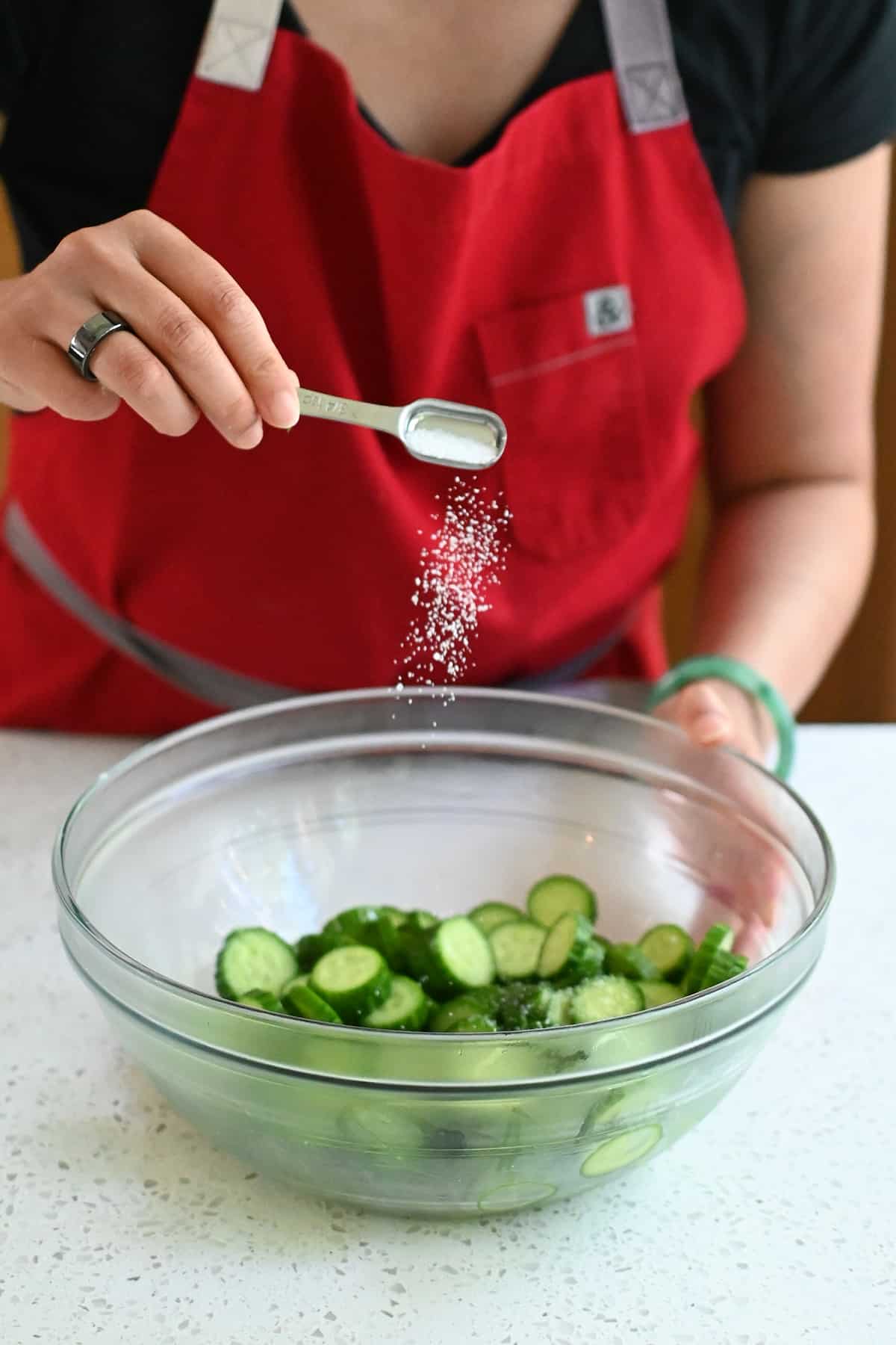 Adding kosher salt to a bowl of sliced Persian cucumbers before making Korean cucumber salad.