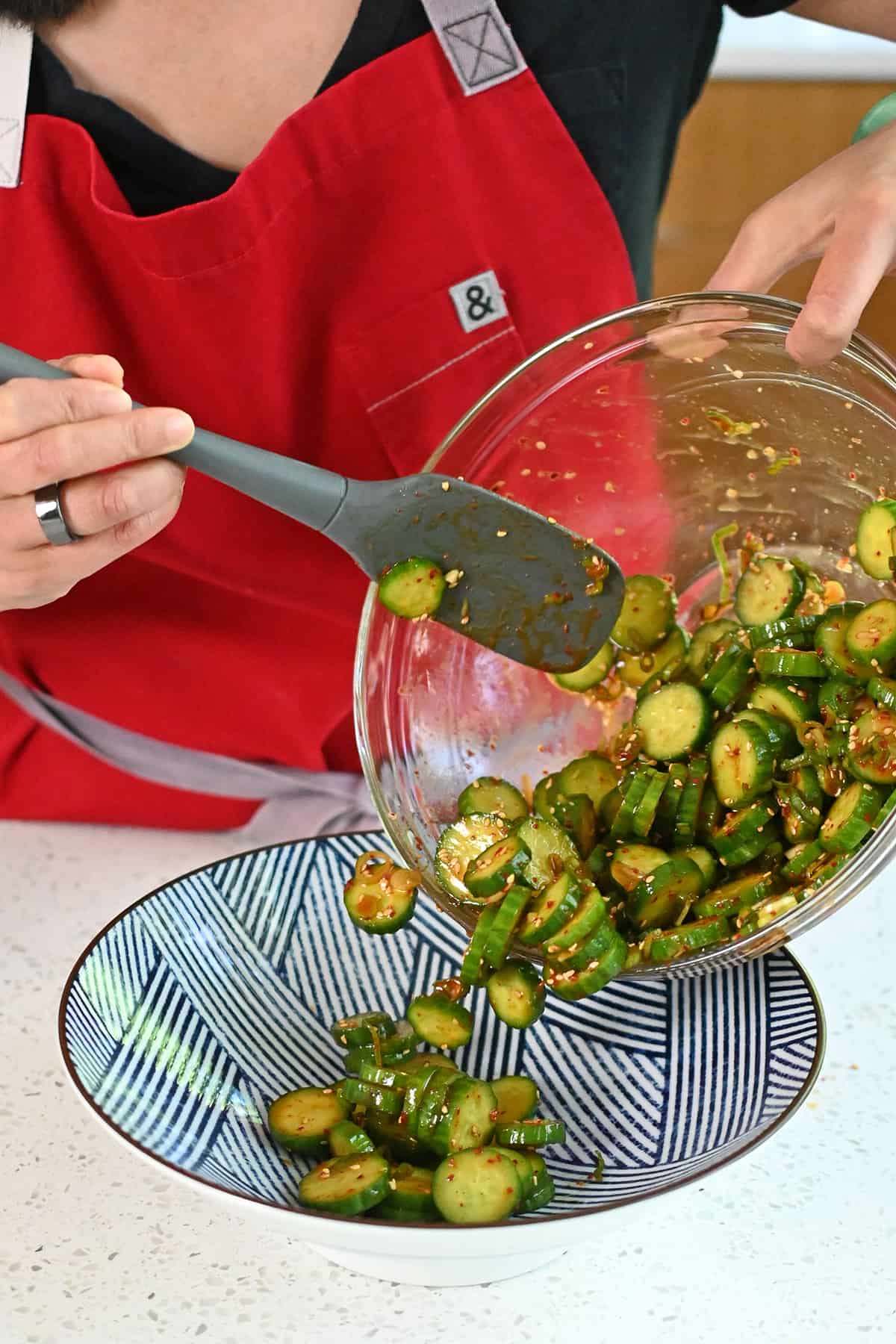 Transferring Korean cucumber salad from a glass mixing bowl to a blue and white serving platter.