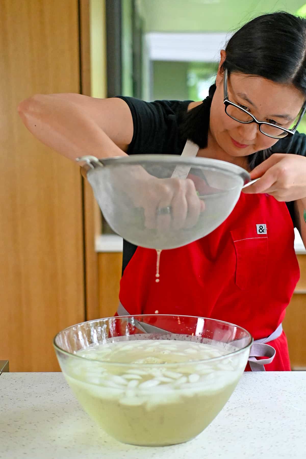 An Asian woman is squeezing the water out of cooked spinach that has been chilled in an ice bath.