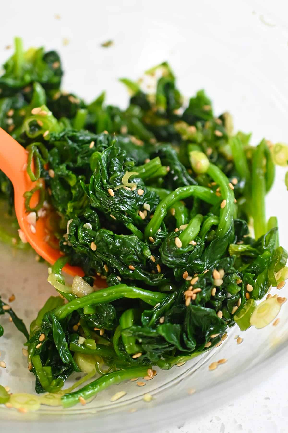A closeup of mixing Korean spinach side dish in a glass bowl with a silicone spatula.