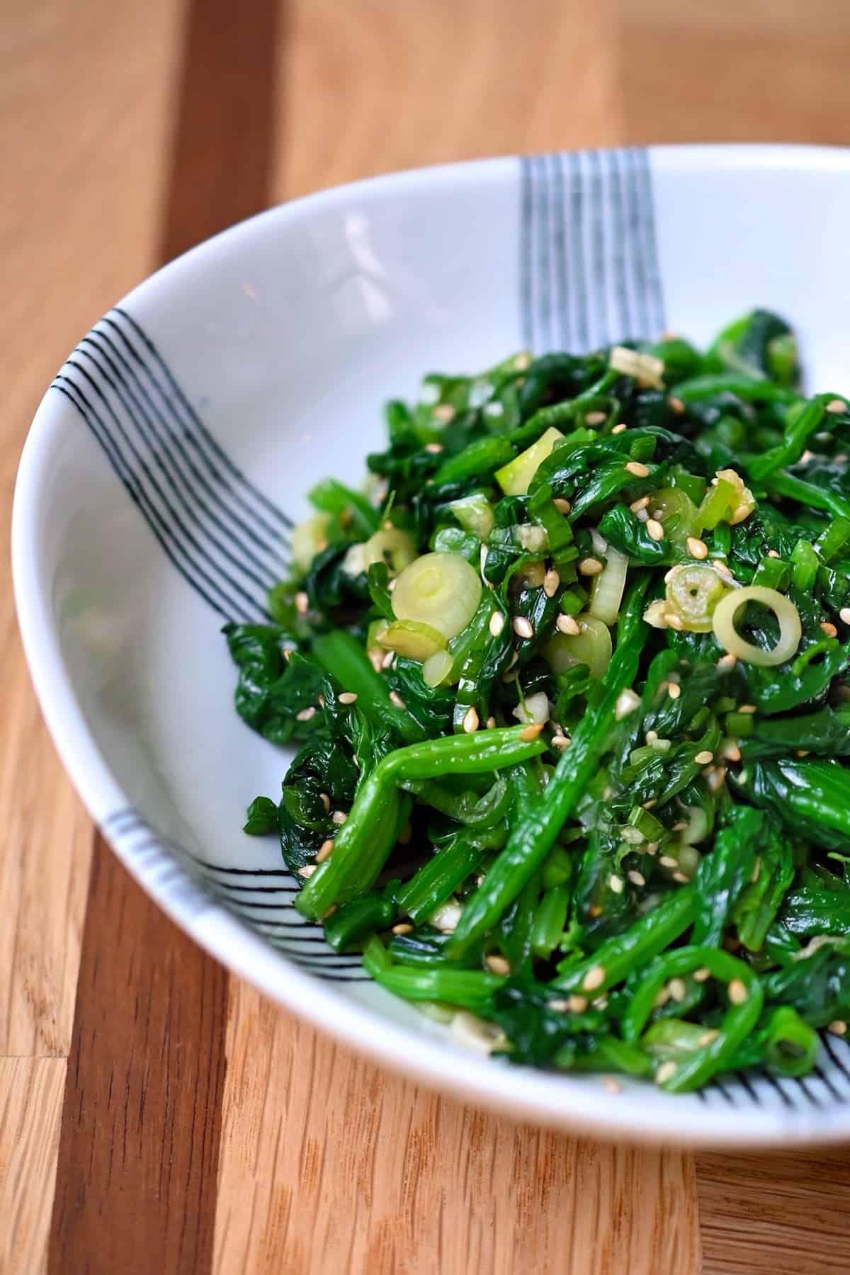An side shot of a white and blue serving bowl filled with Korean spinach side dish.