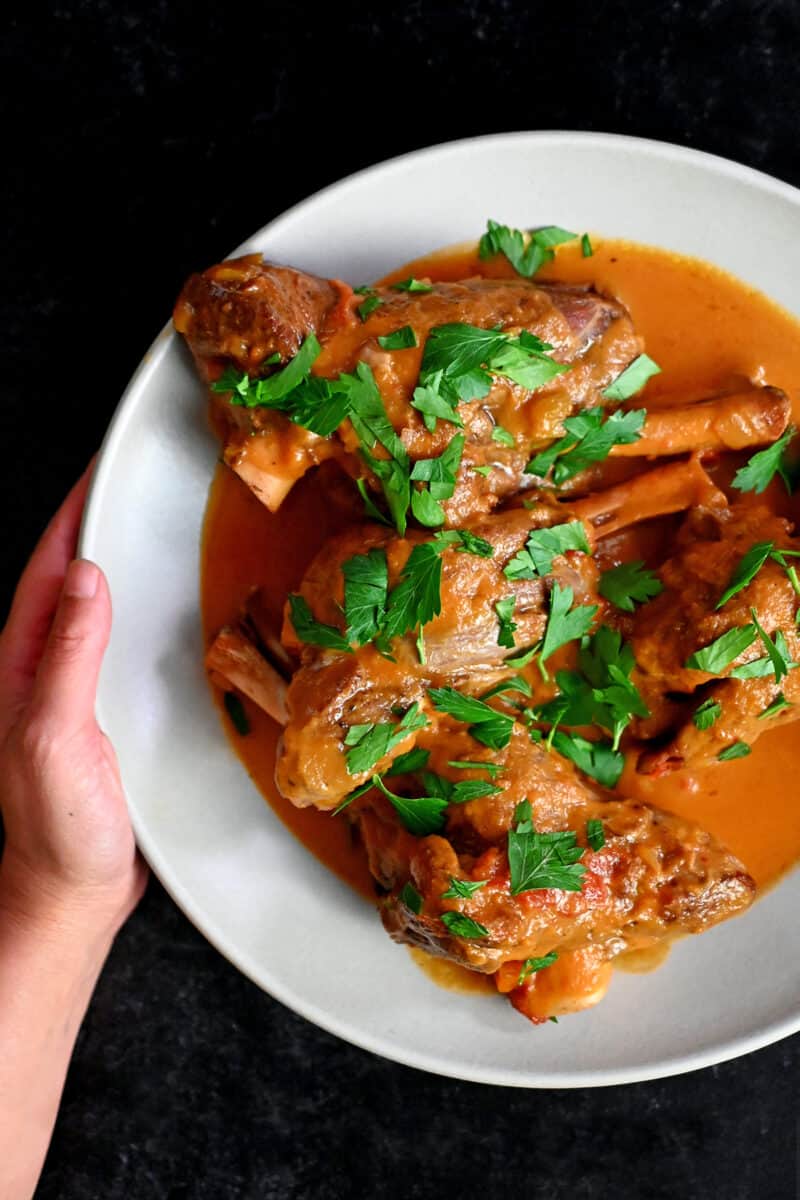A hand holding a white plate with Instant Pot lamb chops ready to eat.