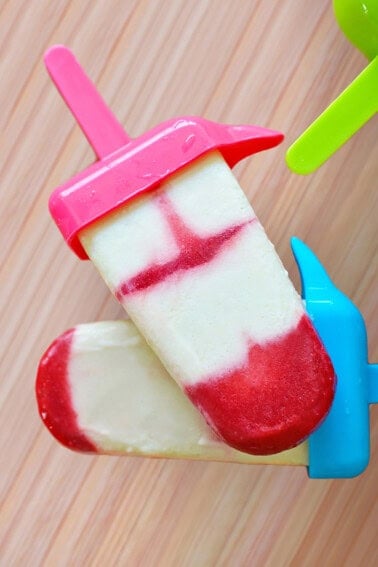 Two red and white homemade popsicles are stacked on top of each other on a wooden surface.