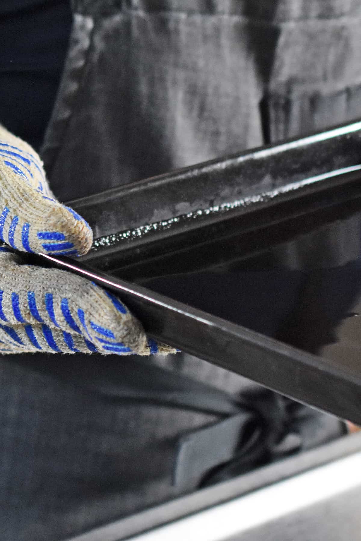 A hand with an oven mitt on is swirling a black rimmed baking sheet with melted ghee inside.