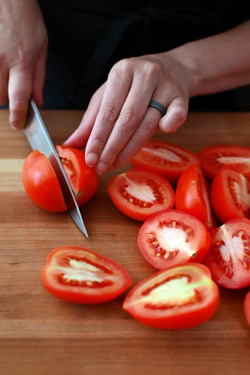 Slicing roma tomatoes in half lengthwise on a wooden cutting board.