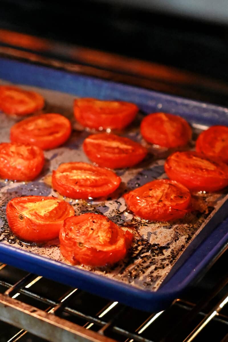 An open oven with a tray of roasted tomatoes inside ready to be taken out.