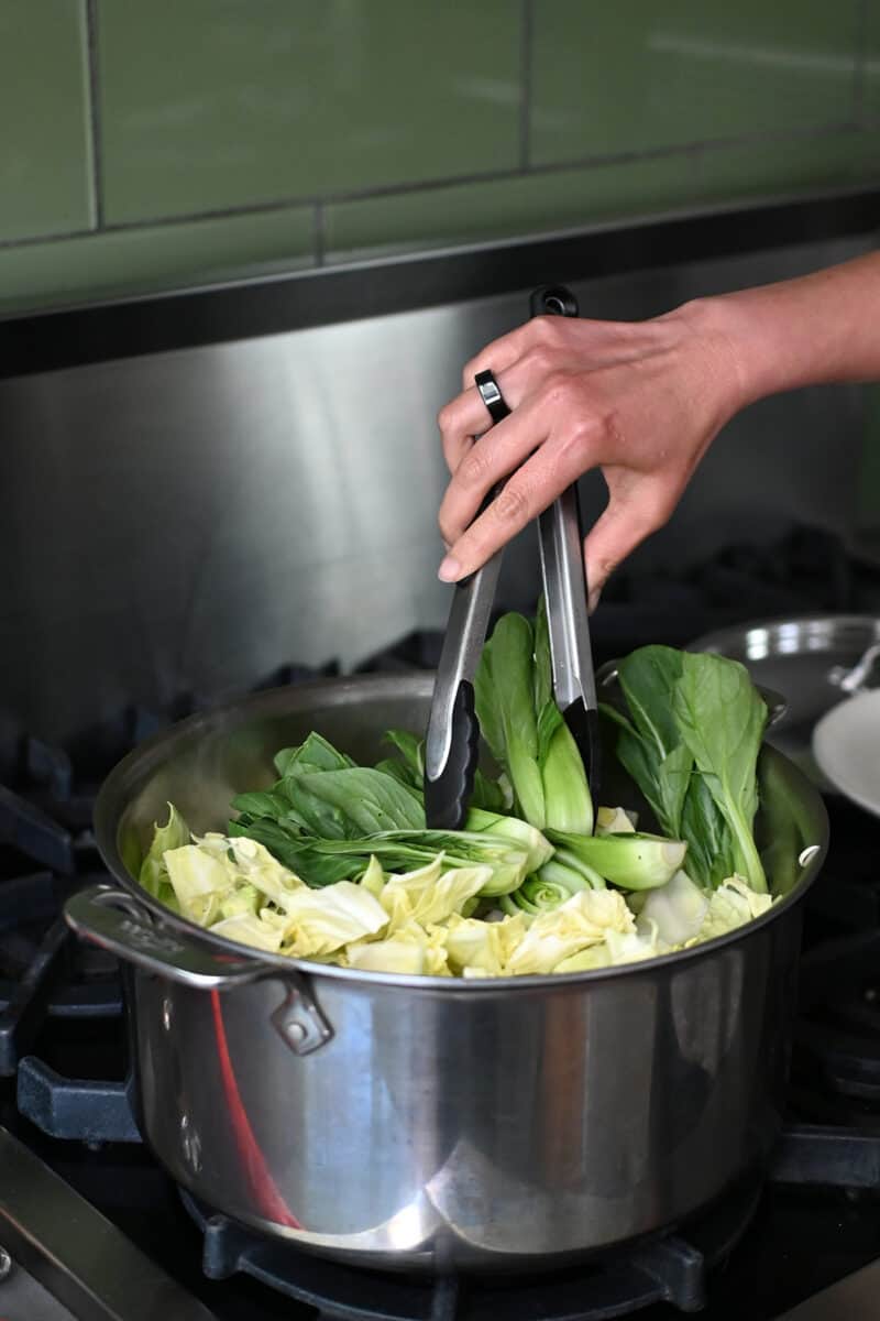 Adding cabbage and bok choy to a pot of oxtail soup.