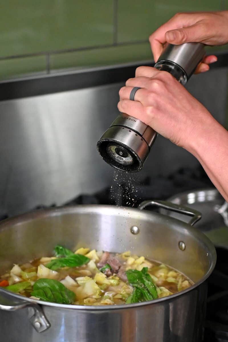 Adding fresh cracked pepper from a Peppermill to a large pot of oxtail soup.