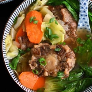An overhead shot of a bowl filled with oxtail soup and vegetables.