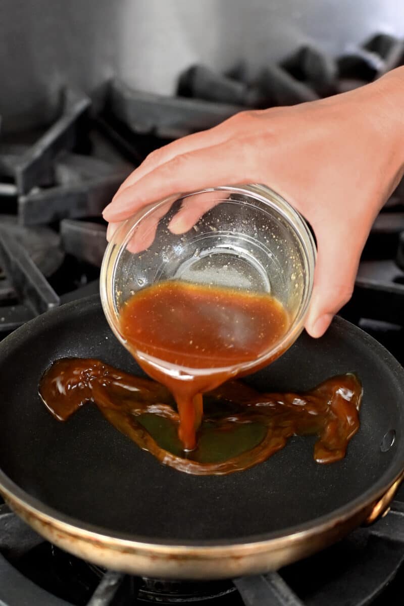 Pouring a small bowl of brown sauce into an small non-stick skillet to make oyakon.