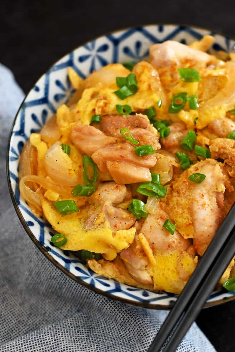 A blue and white bowl of paleo and gluten free oyakodon, a Japanese dish with simmered chicken and scrambled eggs.