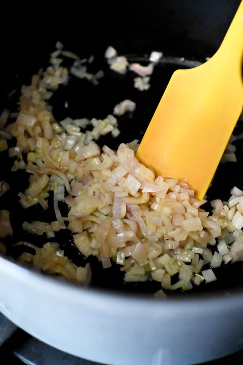 A closeup shot of slightly softened chopped shallots in a gray dutch oven.