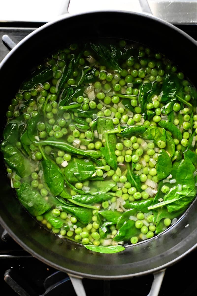 An overhead shot of a pot of pea soup with baby spinach in it right before it is blended.