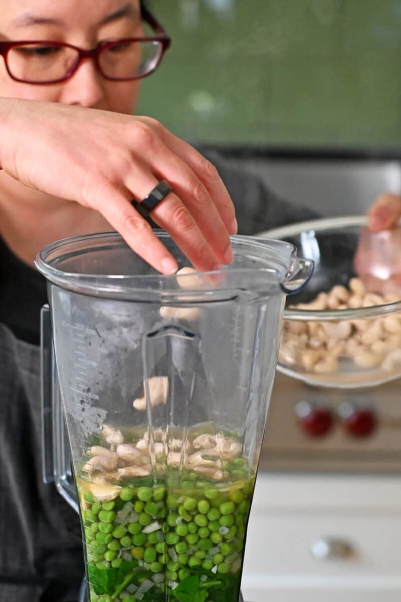 Adding drained cashews to a Vitamix filled with pea soup ready to be blended