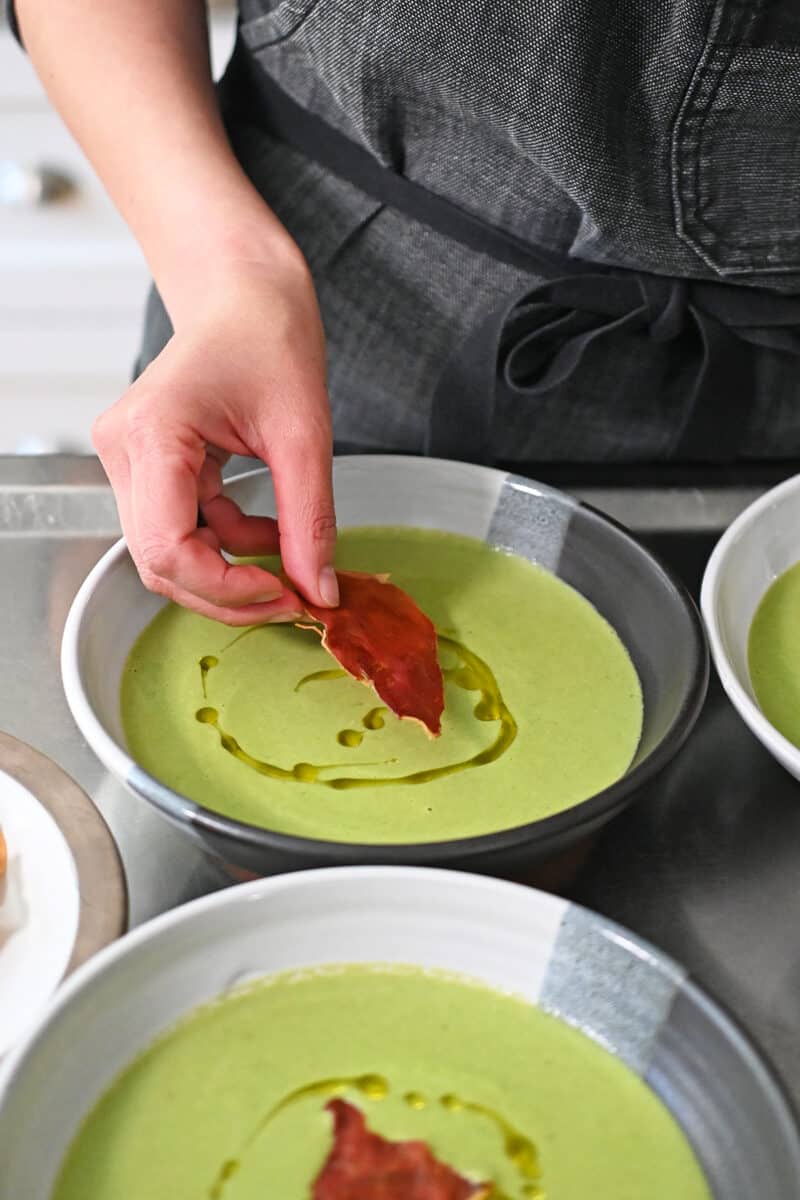 Adding crispy prosciutto chips to bowls of pea soup drizzled with extra virgin olive oil