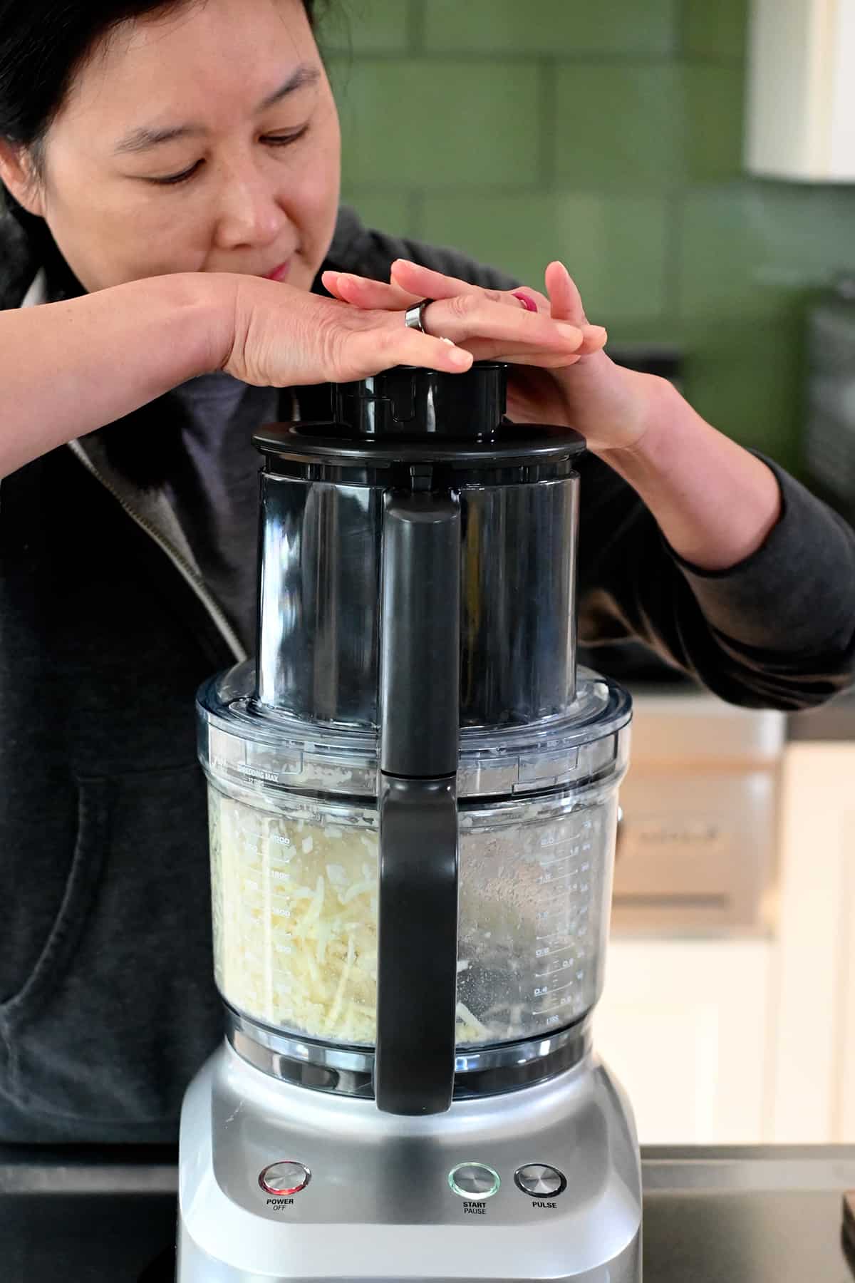An Asian woman is shredding sweet potato in a food processor.