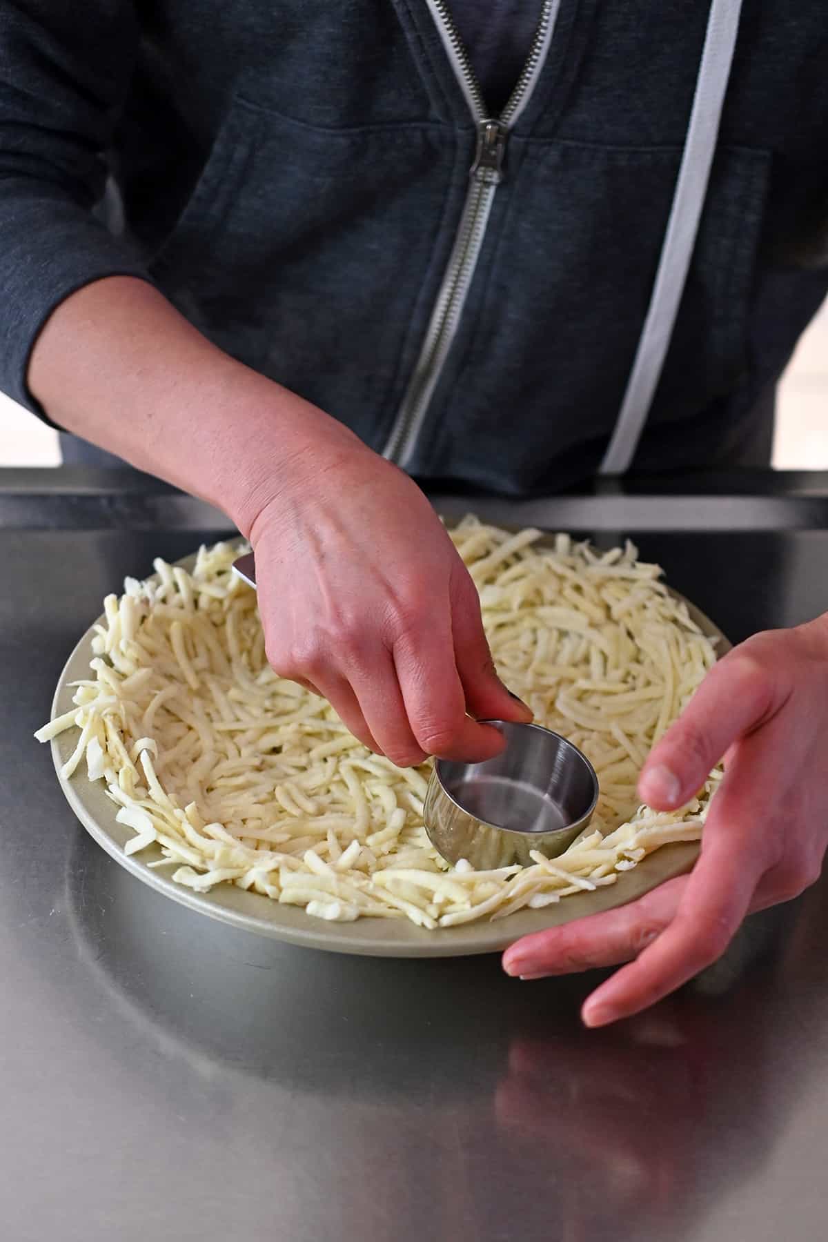 Using a measuring cup to press shredded potatoes into a pie plate.