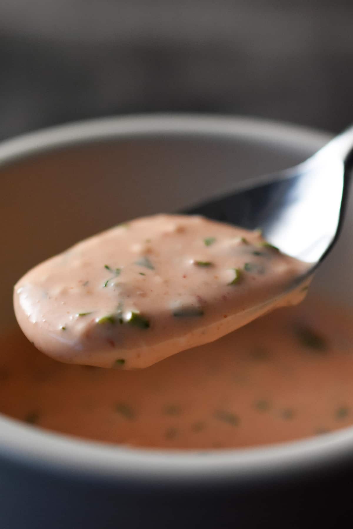 A spoon is scooping some creamy orange homemade sriracha ranch dressing in a white bowl.