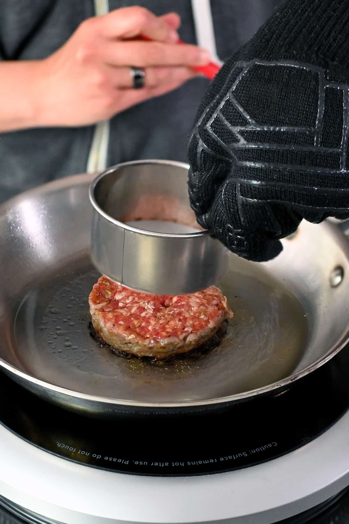 Removing the biscuit cutter to reveal a round sausage patty on a skillet.
