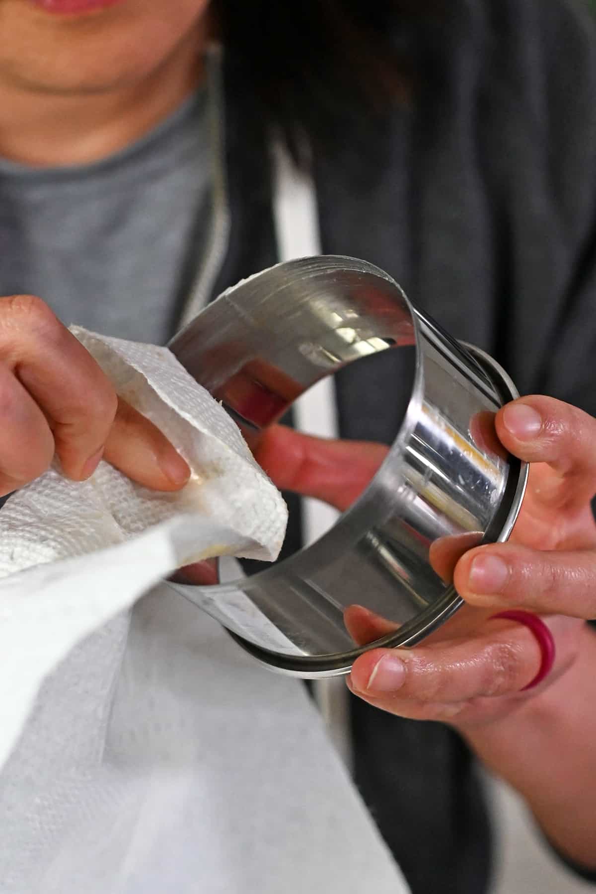 Greasing the inside of a metal biscuit cutter with a paper towel and ghee.