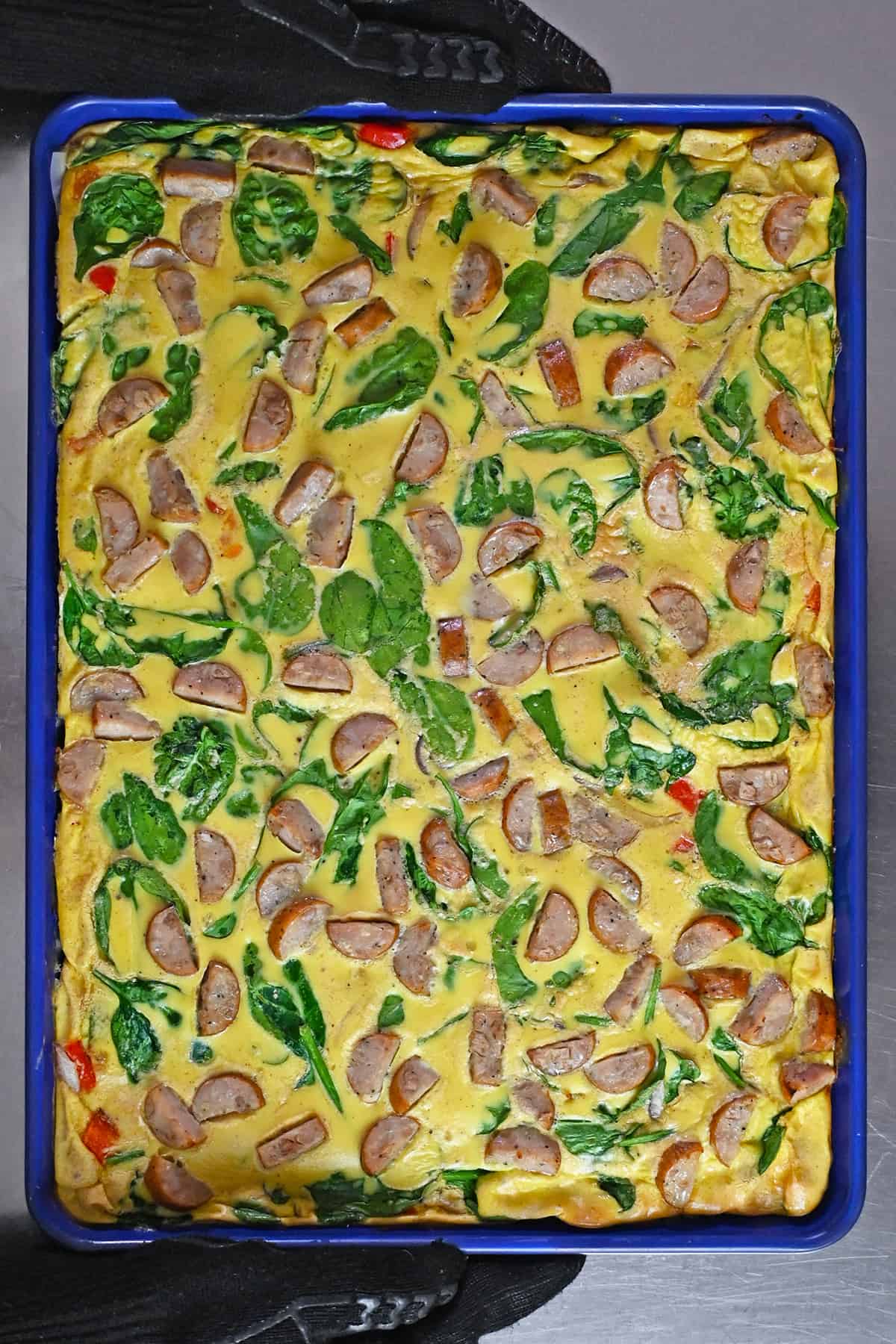 An overhead shot of freshly baked sheet pan eggs with sliced chicken apple sausage, baby spinach, red onions, and bell peppers.