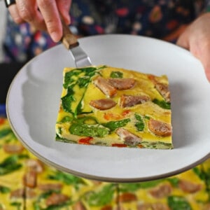 A square slice of sheet pan eggs on a small plate over a pan of sheet pan eggs.