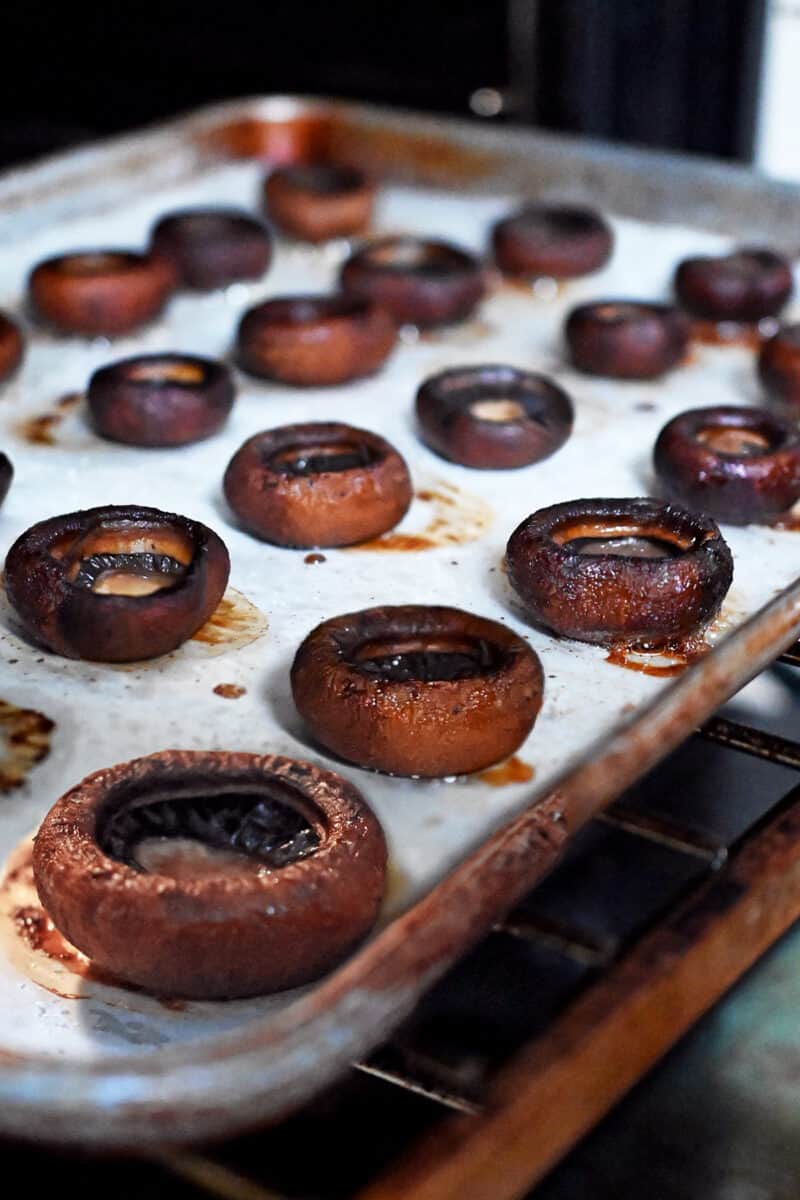 A tray of roasted cremini mushrooms, gill side up.