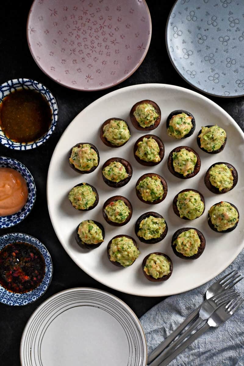 An overhead shot of a plate of shrimp stuffed mushrooms next to some dipping sauces.