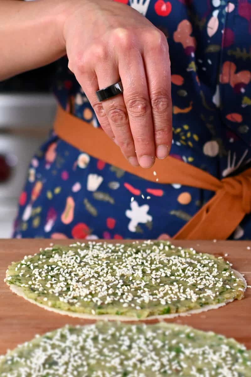 Sprinkling sesame seeds on tortillas topped with a thin layer of shrimp paste.