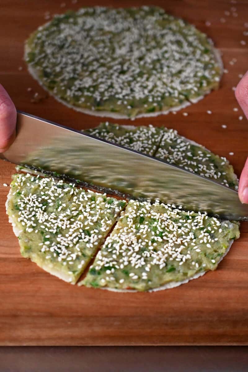 A chef's knife is cutting the raw shrimp toast tortillas into four wedges.