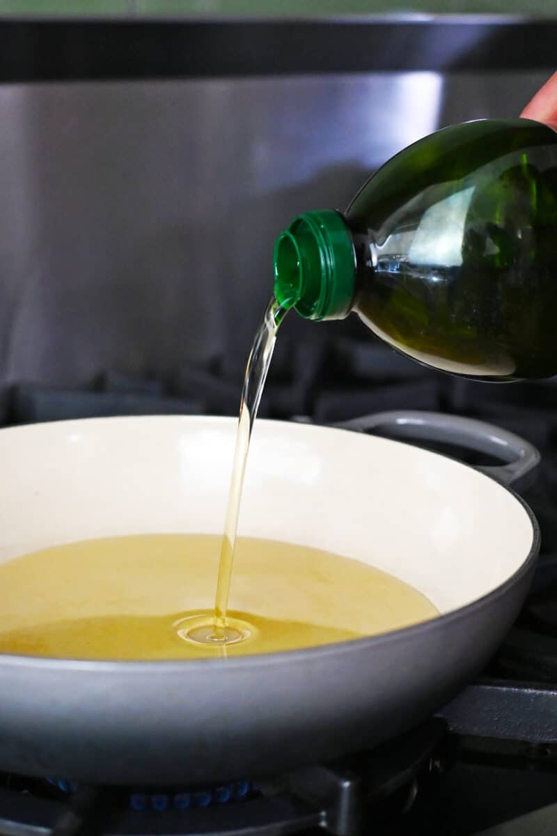 Avocado oil is being poured into a enamel cast iron skillet.