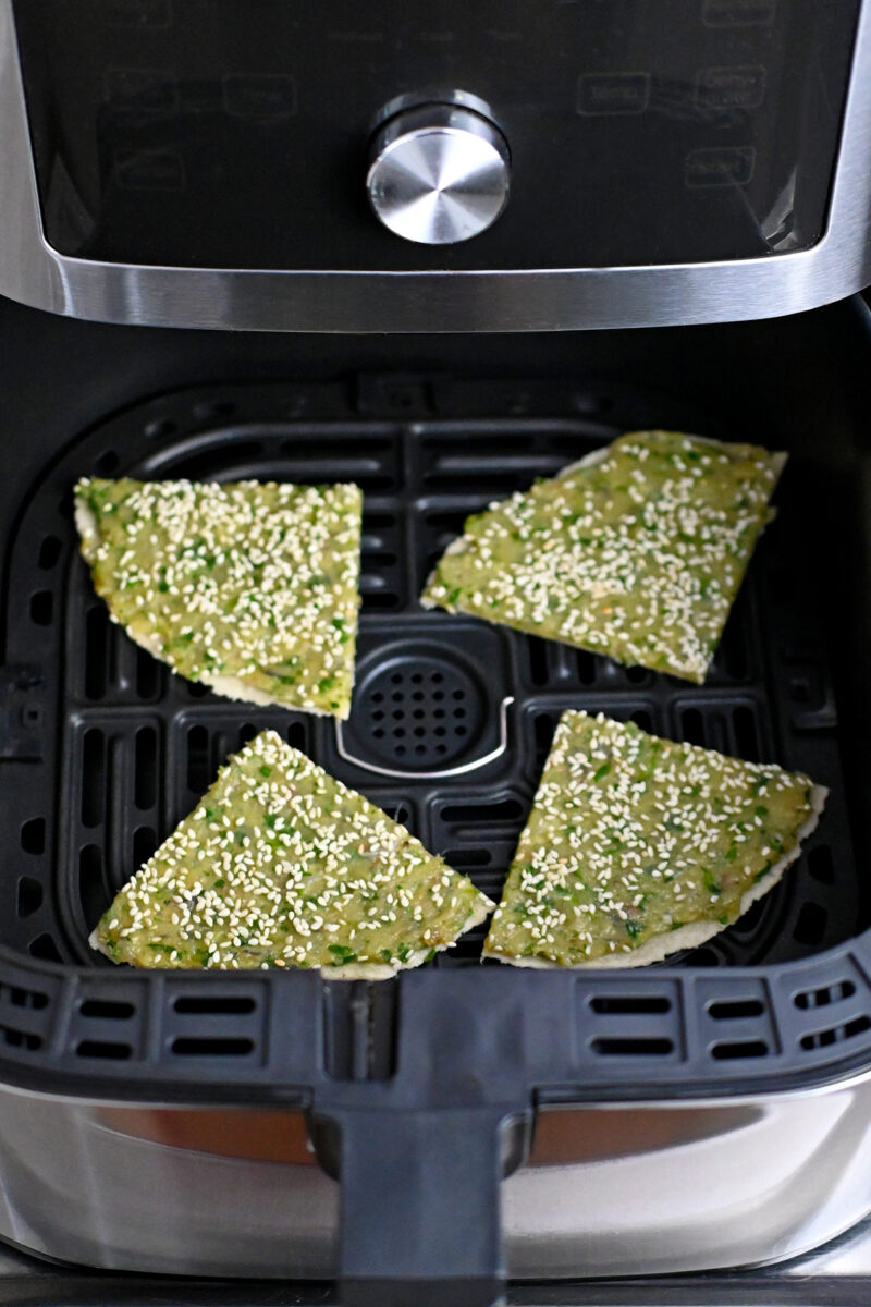 Four wedges of paleo shrimp toast are in an open air fryer about to be cooked.