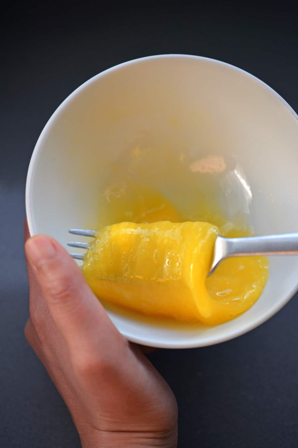 Beating a raw egg in a white bowl with a fork.