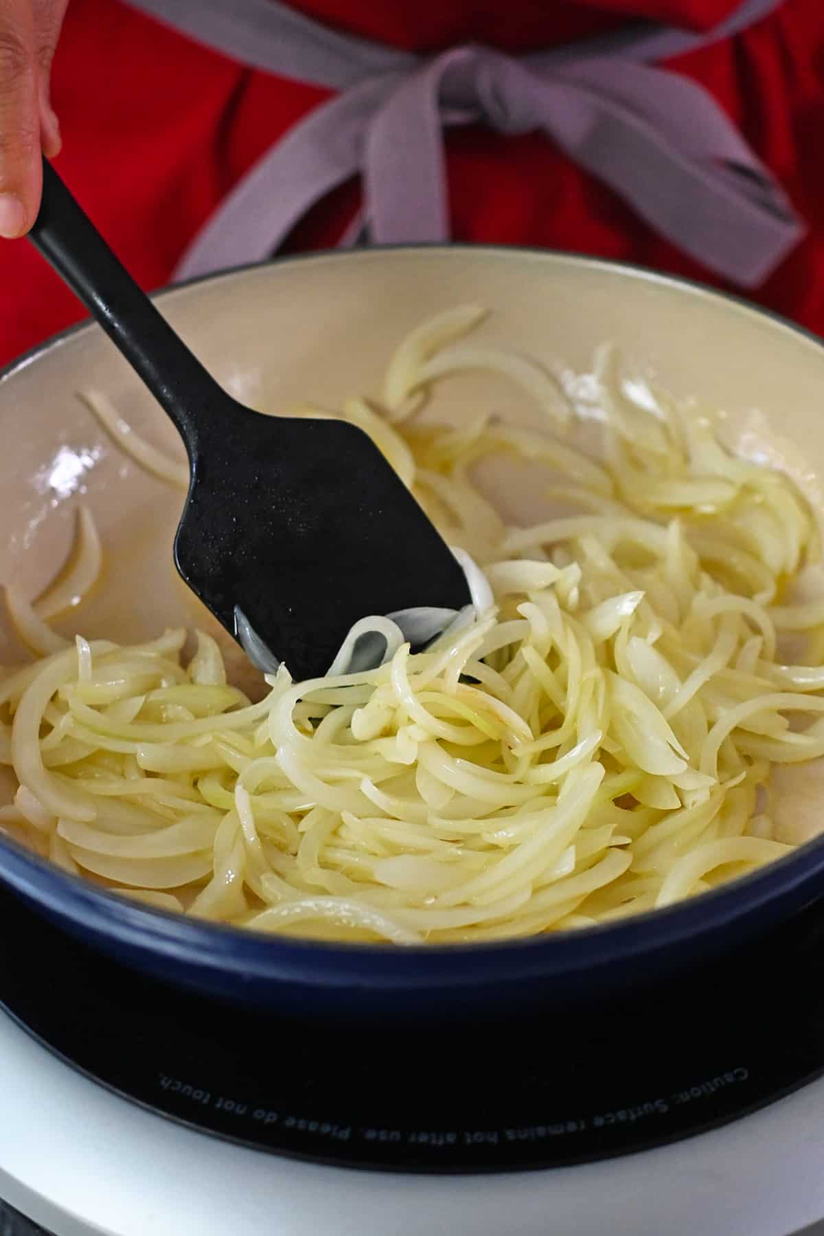 A closeup of sautéed sliced onions in a blue enamel cast iron skillet.