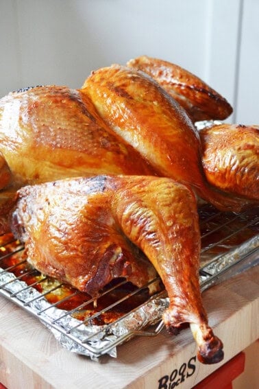 A side view of a golden brown spatchcock turkey resting on a wooden cutting board before it is cut up.