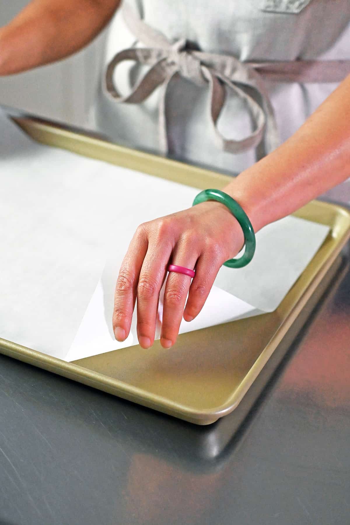 A hand is placing a piece of parchment paper into a rimmed baking sheet.