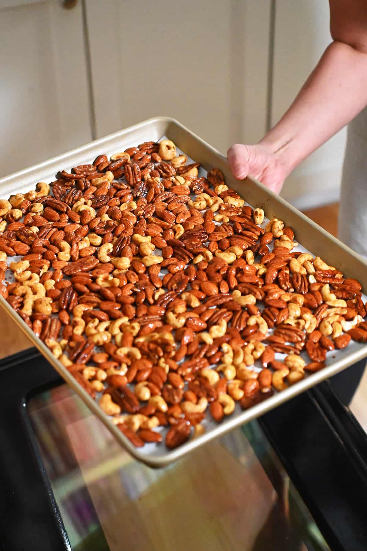 Placing a tray of raw spiced nuts into an open oven.