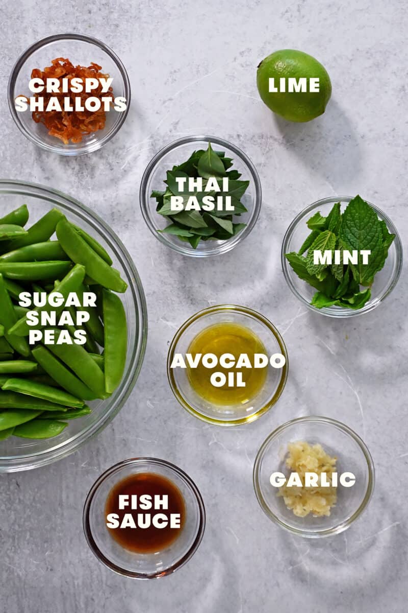 An overhead shot of the raw ingredients for this quick sugar snap pea recipe with garlic, fish sauce, lime juice, fresh herbs, and crispy shallots.