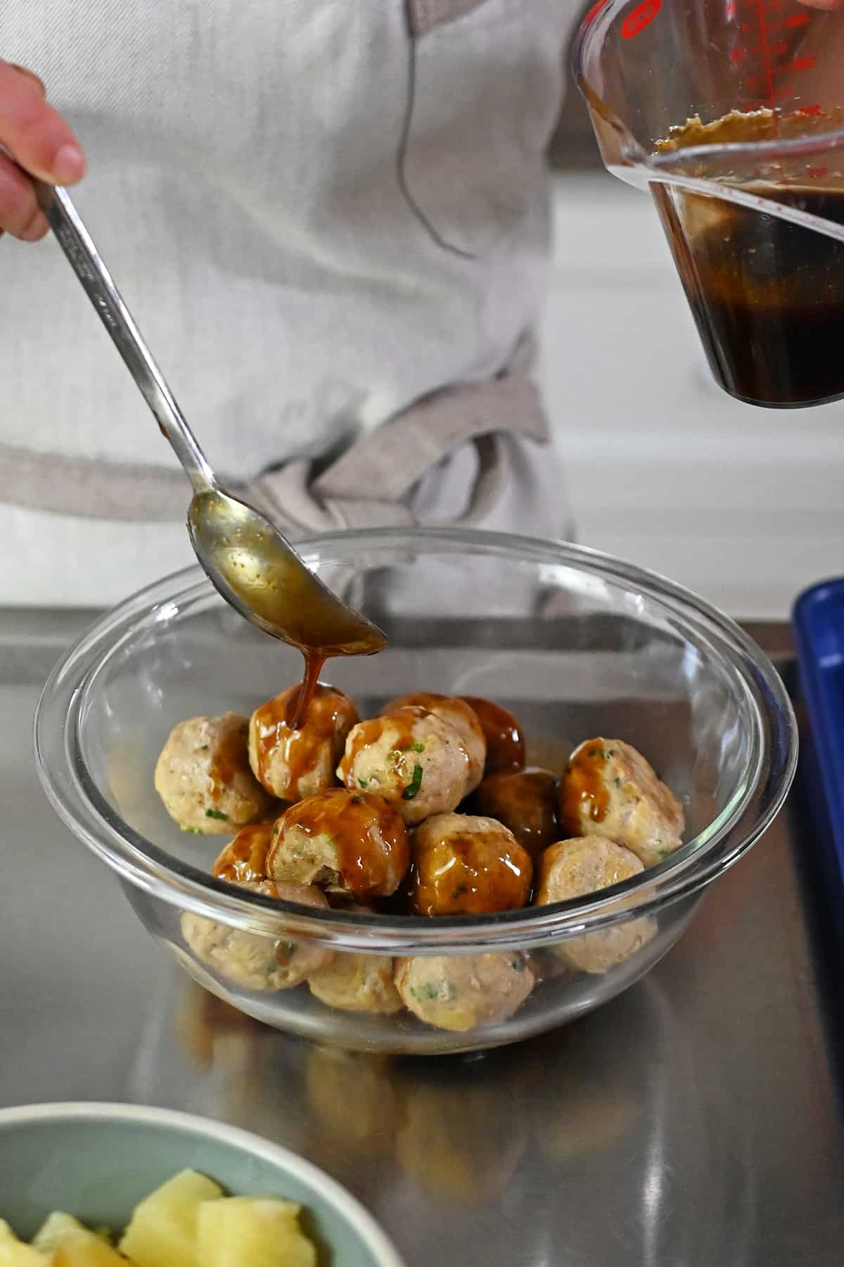 Drizzling paleo teriyaki sauce on a bowl of teriyaki pineapple chicken meatballs.