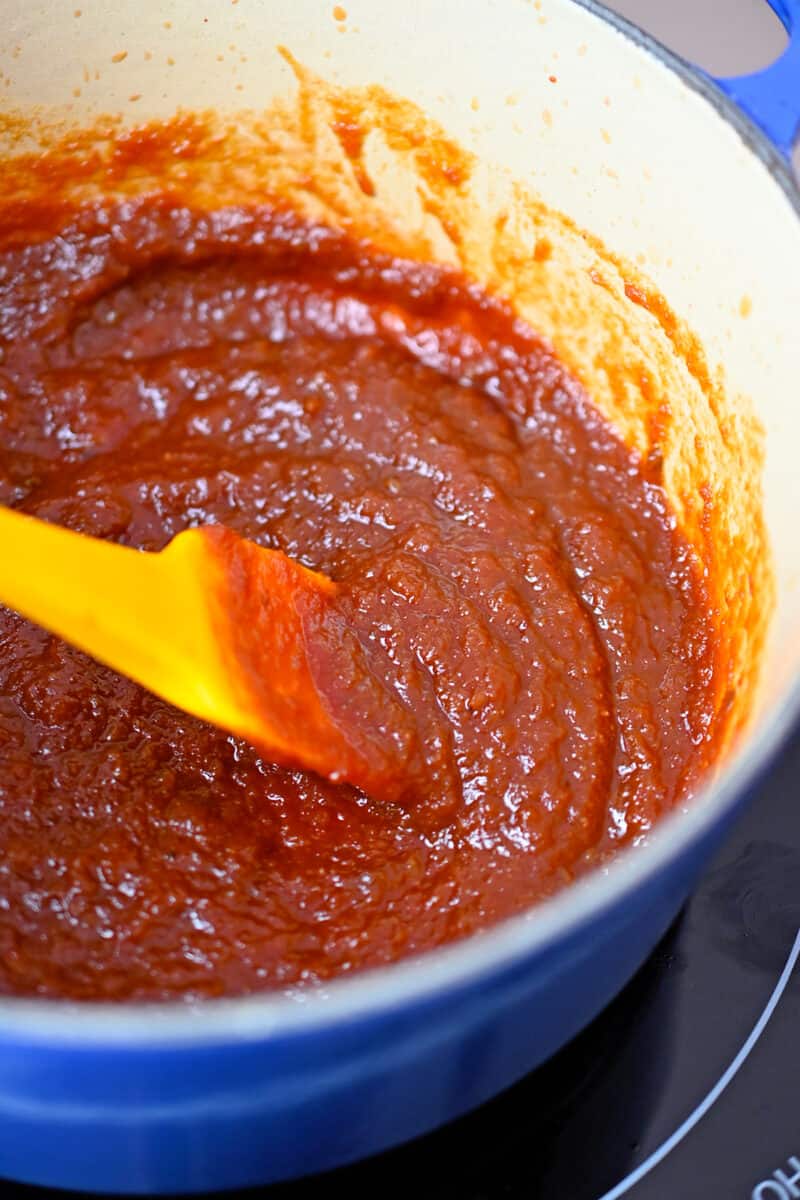 An overhead shot of a thick, simmering reddish brown sauce in a small saucepan.