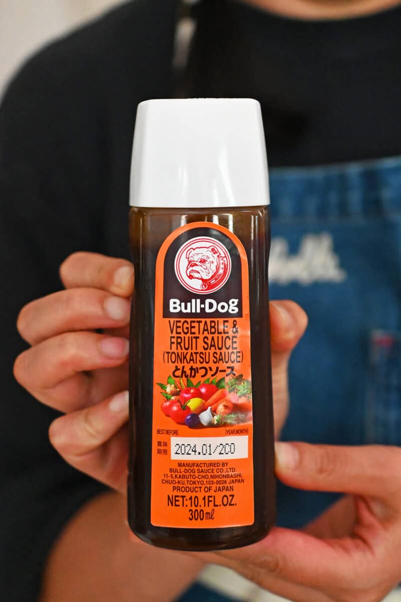 A hand is holding up a bottle of Bulldog Tonkatsu Sauce.