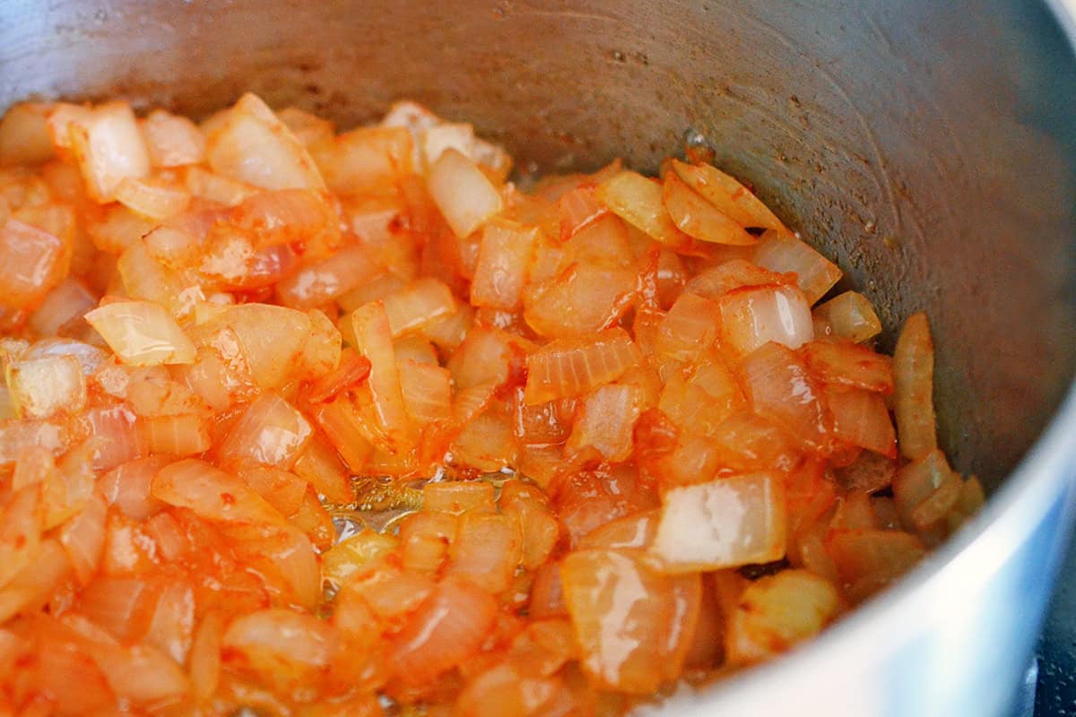 A closeup shot of diced onions and tomato paste cooking in a saucepan, the base of a gluten free gravy.