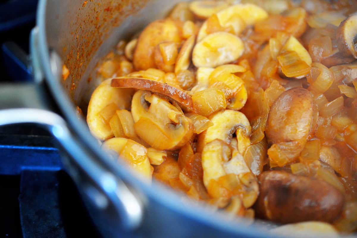 Sautéed sliced button mushrooms and diced onions are cooking in a small saucepan, the base for umami gravy.